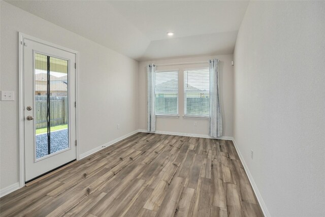 empty room with baseboards, wood finished floors, and vaulted ceiling