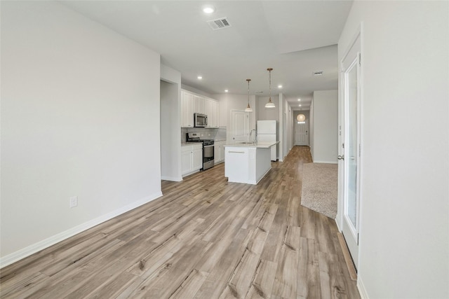 kitchen featuring light wood finished floors, an island with sink, light countertops, white cabinets, and stainless steel appliances