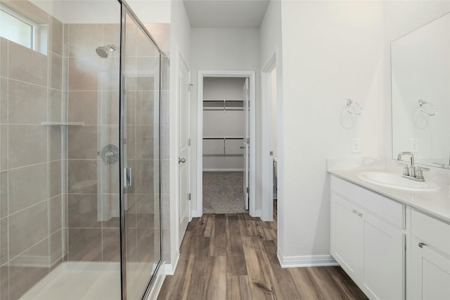 bathroom with vanity, wood finished floors, baseboards, a stall shower, and a walk in closet