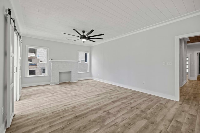 unfurnished living room with light wood-type flooring, crown molding, a brick fireplace, ceiling fan, and a barn door