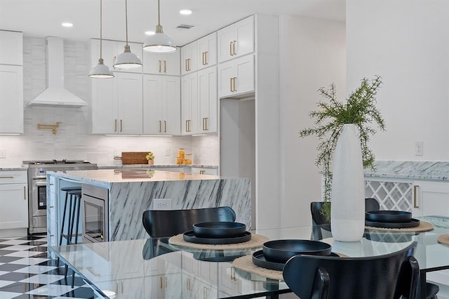 kitchen featuring wall chimney exhaust hood, white cabinetry, backsplash, and high end stainless steel range oven