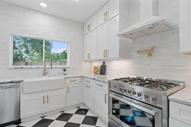 kitchen with appliances with stainless steel finishes, white cabinetry, light stone countertops, wall chimney exhaust hood, and sink