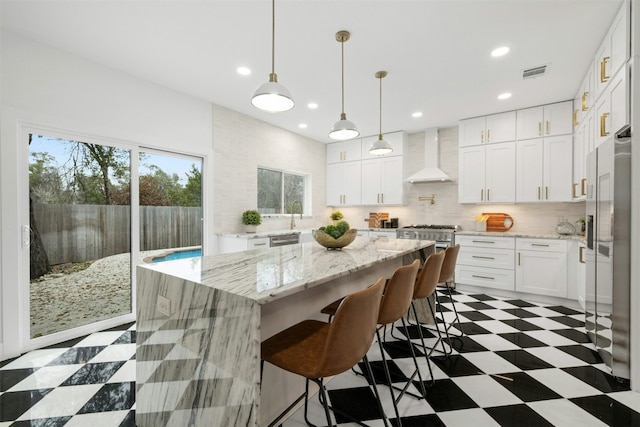 kitchen with wall chimney exhaust hood, appliances with stainless steel finishes, a kitchen island, pendant lighting, and white cabinets