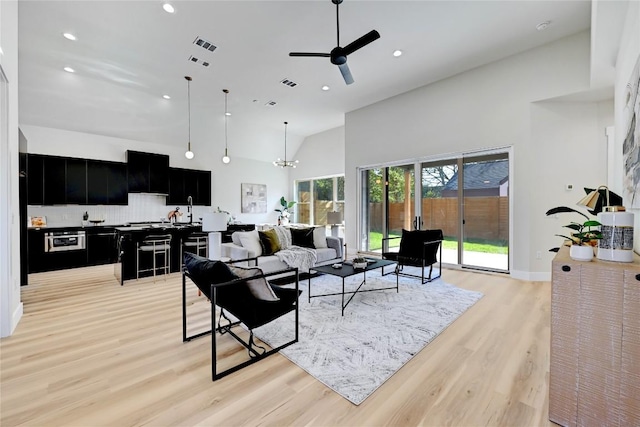 living room featuring ceiling fan with notable chandelier, light wood-type flooring, sink, and a high ceiling