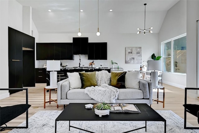 living room featuring high vaulted ceiling, light wood-type flooring, and an inviting chandelier