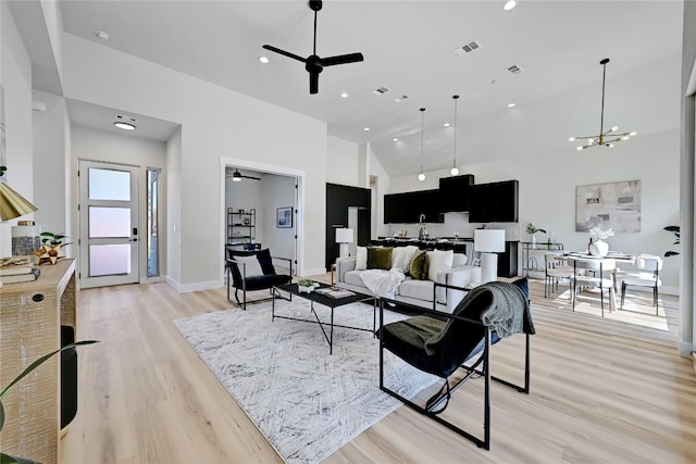 living room featuring high vaulted ceiling, ceiling fan with notable chandelier, and light wood-type flooring