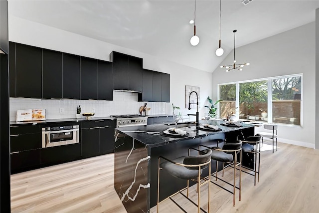 kitchen with stainless steel appliances, hanging light fixtures, light hardwood / wood-style flooring, backsplash, and a spacious island