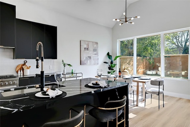 kitchen with backsplash, pendant lighting, an inviting chandelier, light hardwood / wood-style floors, and lofted ceiling