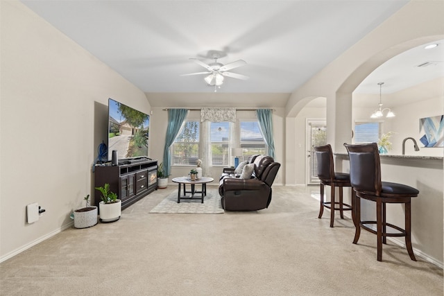 carpeted living room with ceiling fan with notable chandelier