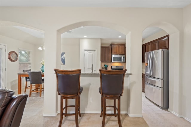 kitchen with light carpet, appliances with stainless steel finishes, a kitchen bar, and stone countertops