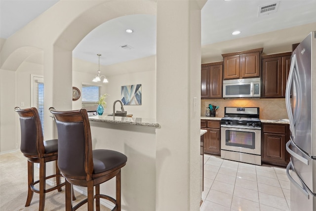 kitchen featuring an inviting chandelier, appliances with stainless steel finishes, a kitchen breakfast bar, pendant lighting, and tasteful backsplash