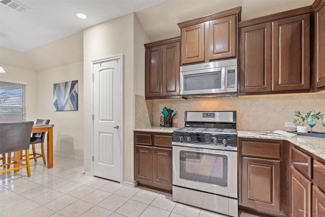 kitchen with appliances with stainless steel finishes, light stone counters, backsplash, and light tile patterned floors