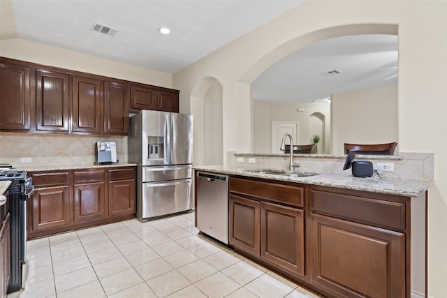 kitchen with backsplash, appliances with stainless steel finishes, sink, light stone counters, and dark brown cabinetry