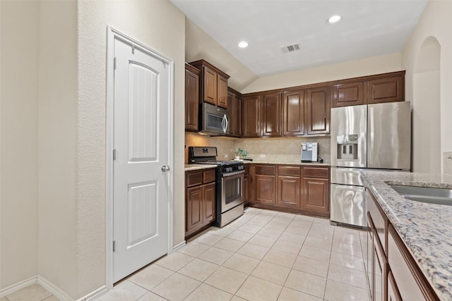 kitchen with light tile patterned floors, vaulted ceiling, appliances with stainless steel finishes, light stone countertops, and tasteful backsplash