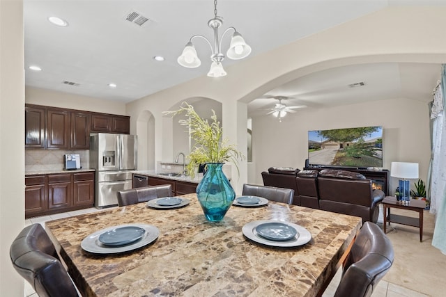 tiled dining room featuring vaulted ceiling, sink, and ceiling fan with notable chandelier