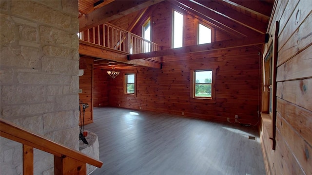 unfurnished room with an inviting chandelier, wooden walls, high vaulted ceiling, and wood finished floors