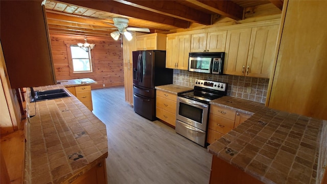 kitchen featuring ceiling fan with notable chandelier, appliances with stainless steel finishes, tile counters, and light hardwood / wood-style flooring