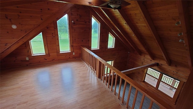 additional living space with vaulted ceiling with beams, wood ceiling, wood walls, ceiling fan, and light wood-type flooring