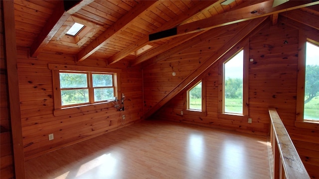 additional living space with light hardwood / wood-style flooring, wooden walls, and lofted ceiling with skylight