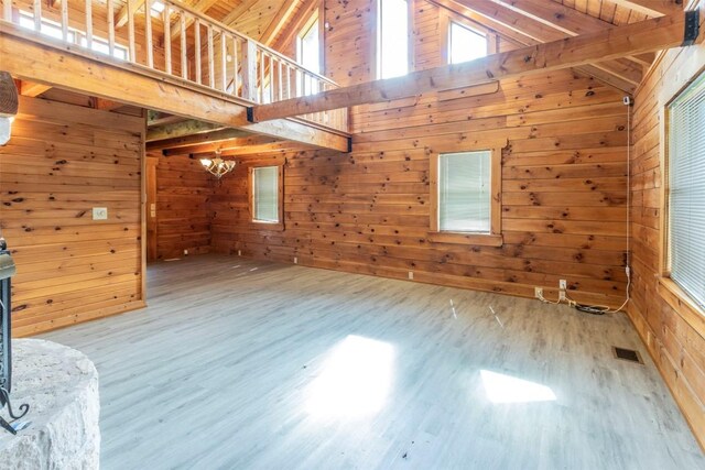 unfurnished living room with wood walls, beamed ceiling, wood-type flooring, high vaulted ceiling, and a chandelier