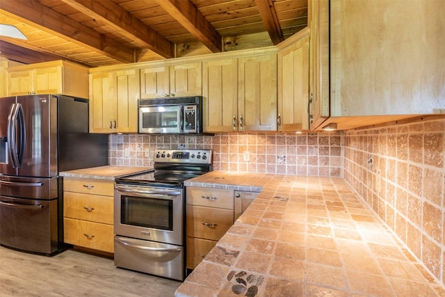 kitchen with beamed ceiling, tile countertops, wooden ceiling, appliances with stainless steel finishes, and light brown cabinets