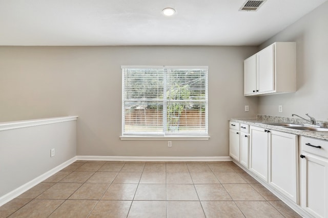 kitchen featuring white cabinets, light stone countertops, light tile patterned floors, and sink