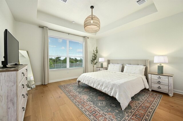 bedroom featuring a raised ceiling and light hardwood / wood-style flooring