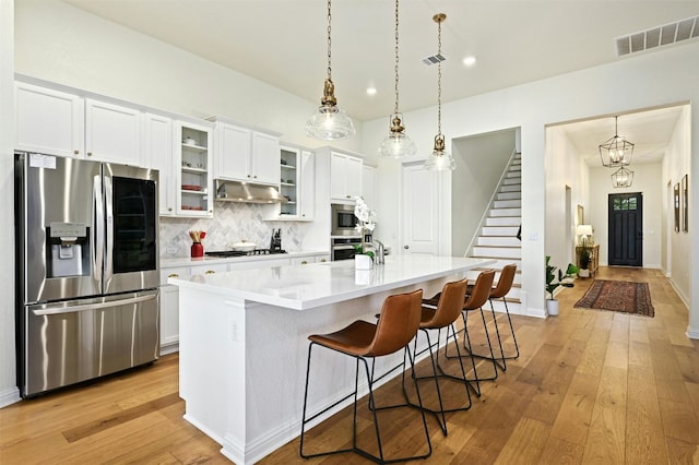 kitchen with appliances with stainless steel finishes, backsplash, white cabinets, a kitchen breakfast bar, and a kitchen island with sink