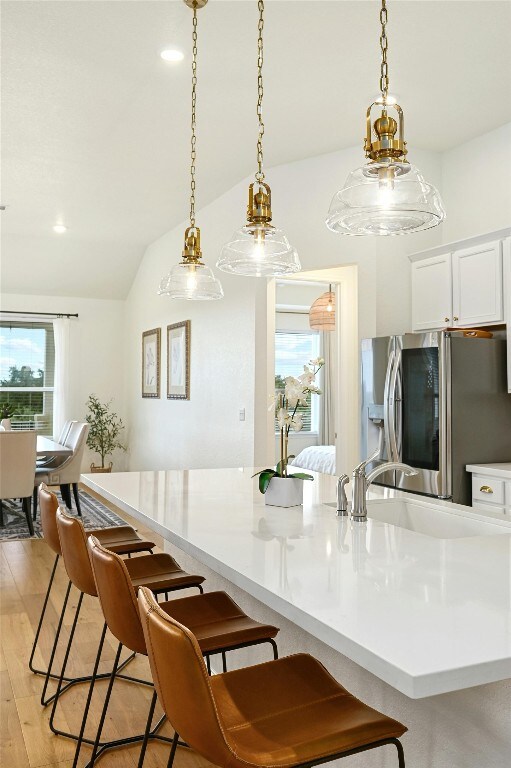 kitchen with stainless steel refrigerator, decorative light fixtures, sink, and vaulted ceiling