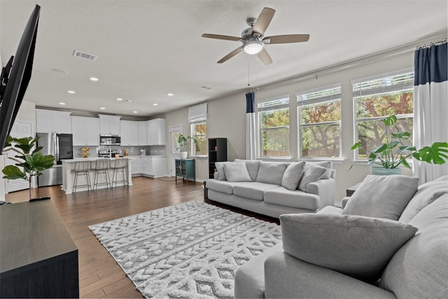 living room featuring ceiling fan, a textured ceiling, and dark hardwood / wood-style flooring