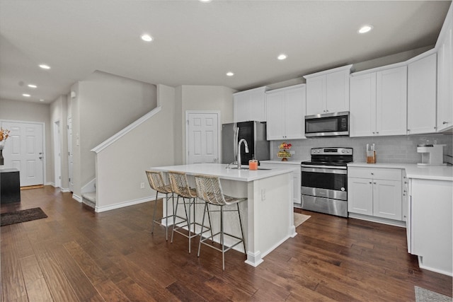 kitchen featuring dark wood-type flooring, appliances with stainless steel finishes, a center island with sink, and white cabinets