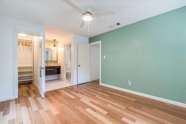 unfurnished bedroom featuring a walk in closet, ceiling fan, light wood-type flooring, connected bathroom, and a closet