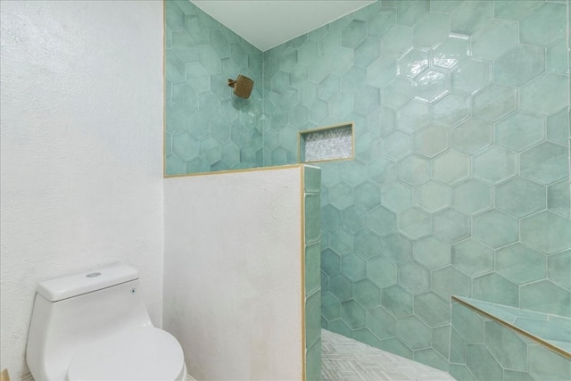 full bathroom with a tile shower and toilet