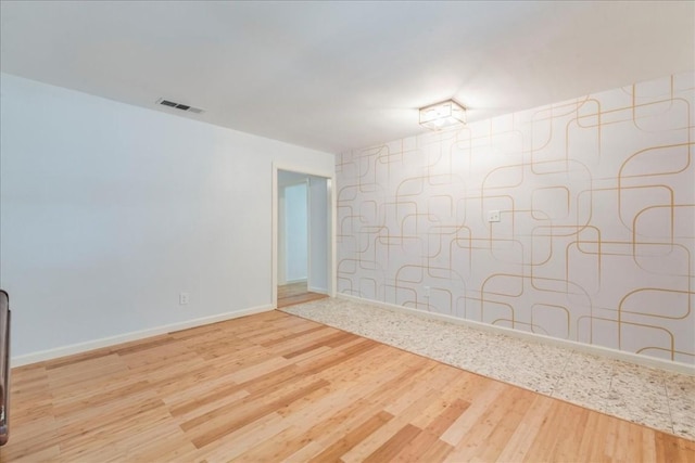 empty room featuring light wood-type flooring, visible vents, and baseboards