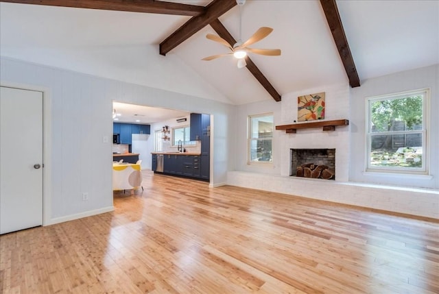 unfurnished living room featuring light wood finished floors, a ceiling fan, lofted ceiling with beams, a brick fireplace, and a sink