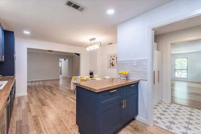 kitchen featuring blue cabinetry, light floors, visible vents, backsplash, and butcher block countertops