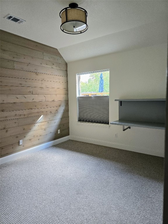 empty room with vaulted ceiling, carpet floors, and wooden walls