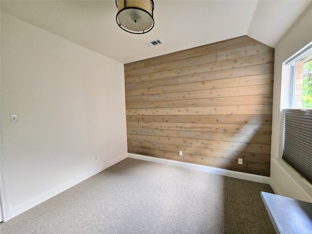 empty room featuring wooden walls, carpet, and vaulted ceiling