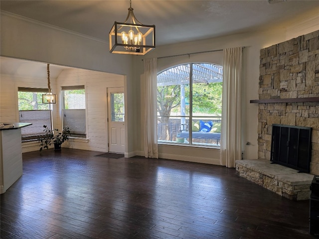 unfurnished living room with dark wood-type flooring, a fireplace, crown molding, and a notable chandelier