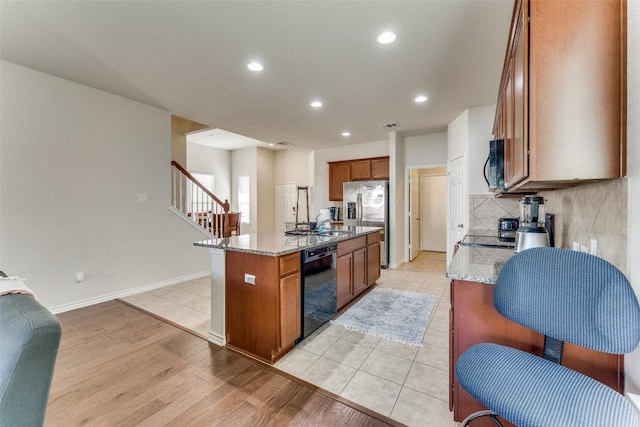 kitchen with light stone countertops, an island with sink, recessed lighting, brown cabinetry, and dishwasher