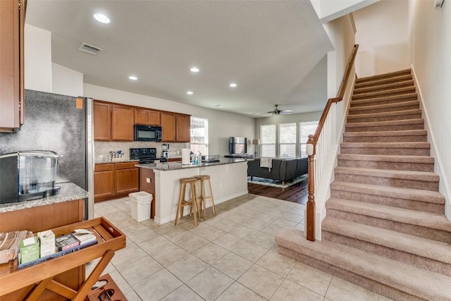 kitchen featuring a kitchen bar, ceiling fan, a kitchen island with sink, black appliances, and light tile patterned floors