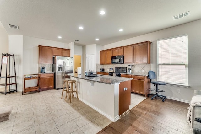 kitchen featuring visible vents, black appliances, backsplash, and brown cabinetry
