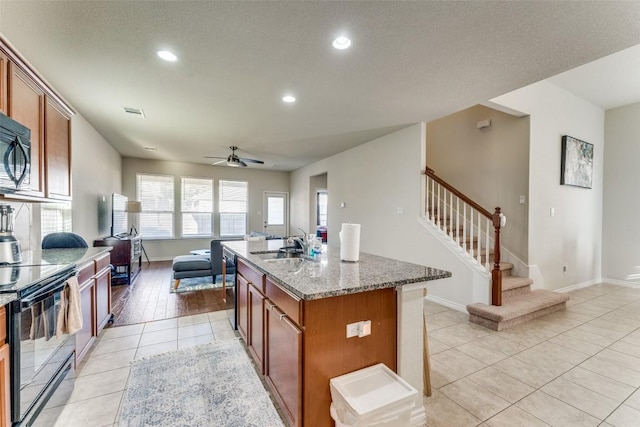 kitchen with light stone countertops, ceiling fan, light tile patterned floors, a center island with sink, and black / electric stove