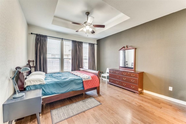 bedroom with a raised ceiling, a ceiling fan, light wood-style floors, and a textured wall
