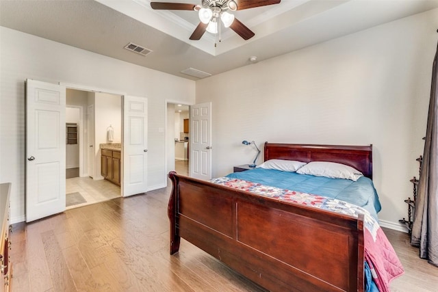 bedroom with a raised ceiling, ensuite bathroom, light hardwood / wood-style flooring, and ceiling fan