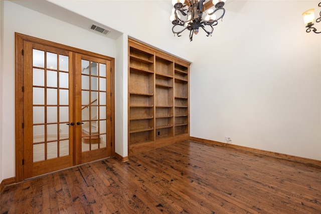 empty room featuring dark hardwood / wood-style flooring, a chandelier, and french doors