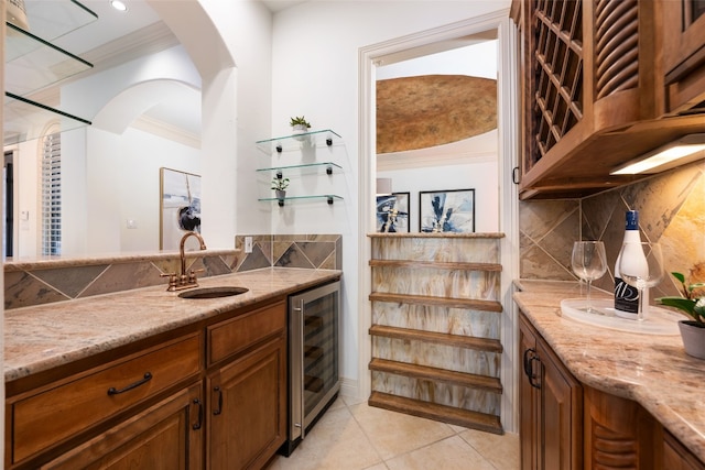 kitchen featuring light tile patterned flooring, crown molding, light stone countertops, sink, and beverage cooler