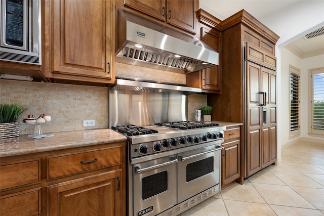 kitchen featuring light stone counters, built in appliances, light tile patterned floors, crown molding, and backsplash