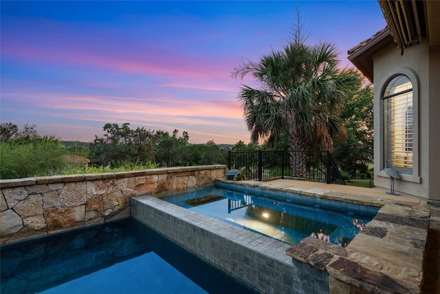 pool at dusk with a patio and an in ground hot tub