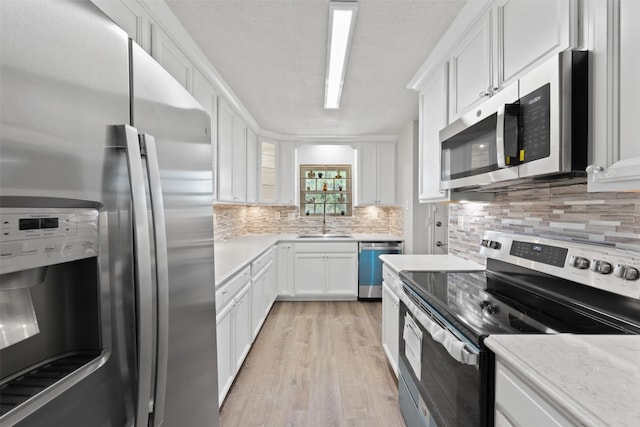 kitchen featuring white cabinetry, light hardwood / wood-style flooring, backsplash, sink, and appliances with stainless steel finishes